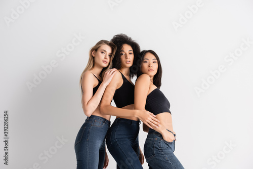 interracial women in tops and denim jeans posing on white