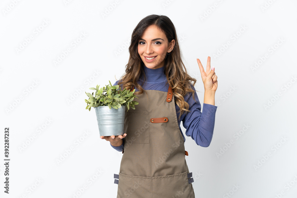 Gardener girl holding a plant isolated on white background smiling and showing victory sign Gardener girl holding a plant isolated on white background smiling and showing victory sign
