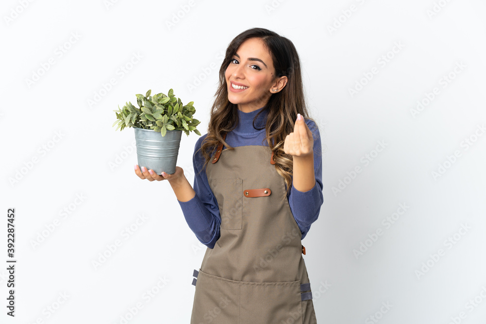 Gardener girl holding a plant isolated on white background making money gesture Gardener girl holding a plant isolated on white background making money gesture