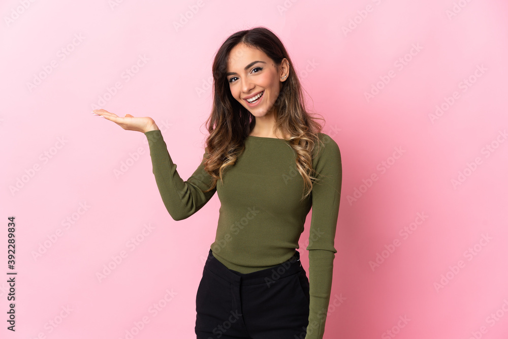 Young caucasian woman isolated on pink background holding copyspace imaginary on the palm to insert an ad Young caucasian woman isolated on pink background holding copyspace imaginary on the palm to insert an ad