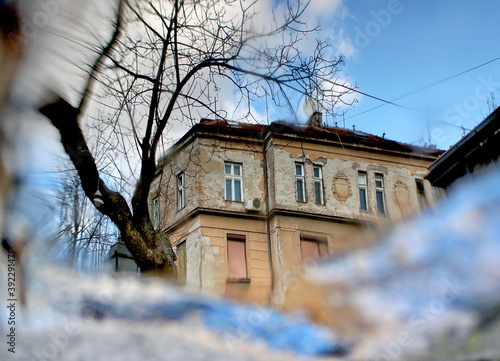 Reflection of the sky with clouds, residential building and tree branches in puddle,blur © zonik1