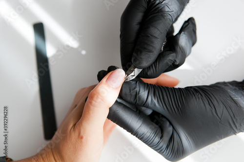  a master in black gloves makes a classic manicure with pliers for a girl. female hands with white and yellow gold rings