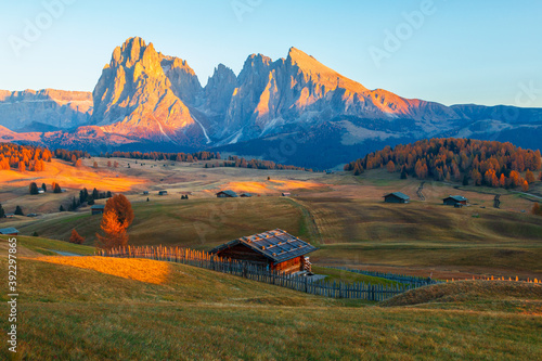 Mountain meadow and wood house Alpe di Siusi or Seiser Alm in the background Langkofel mountain range at beautiful sunset with Province of Bolzano, South Tyrol in Dolomites photo