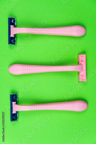 Three pink disposable razors on a green . Personal hygiene items for shaving.
