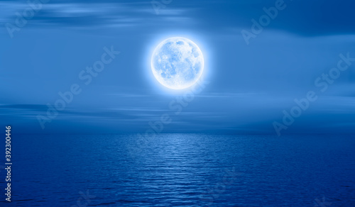 Night sky with full bright moon in the clouds  blue sea in the foreground  Elements of this image furnished by NASA