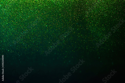 Christmas light background. Sparkling magical dust particles. Falling glitters on green background. 