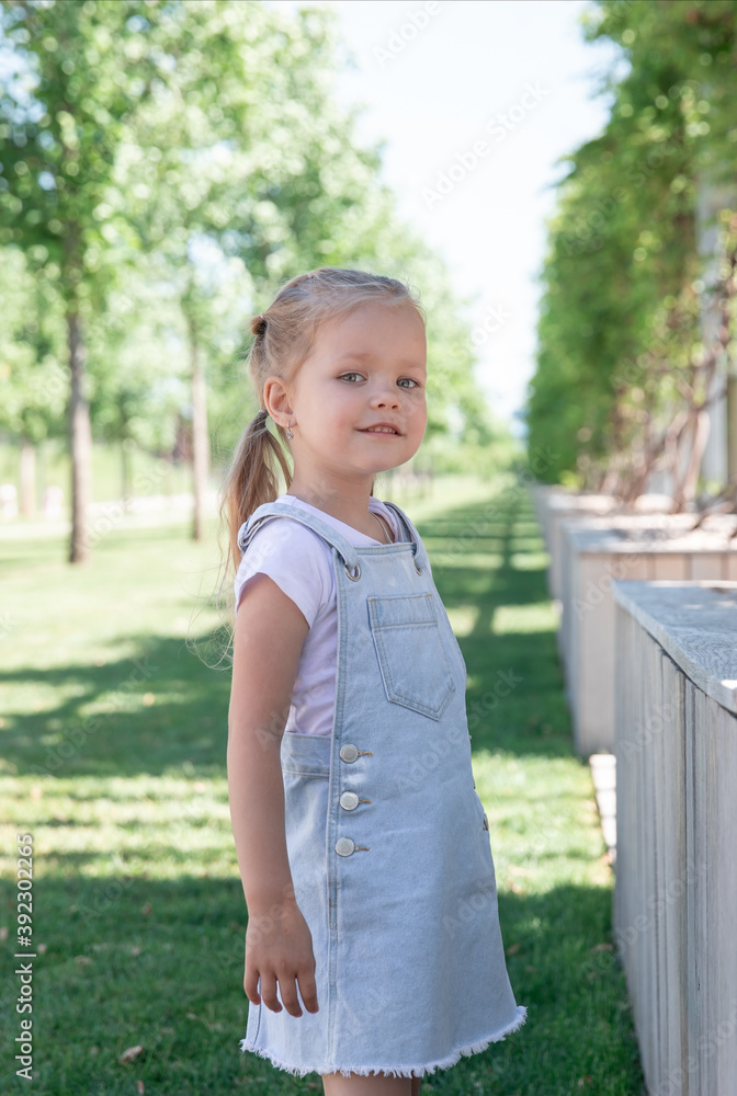 little girl blonde 5 years old in denim sarafan walks around the park. little girl blonde 5 years old in denim sarafan walks around the park.