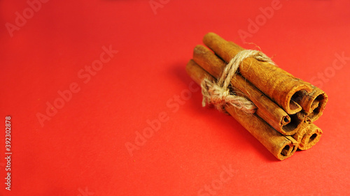 five brown cinnamon sticks tied with thread on a red background side view . Christmas symbols and spices
