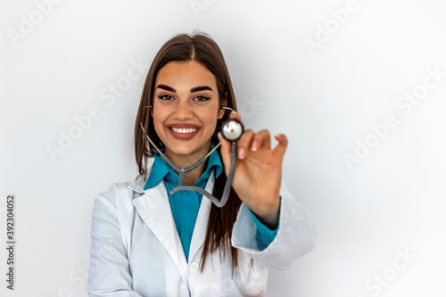 Pretty young doctor holding up stethoscope and smiling at camera. Nurse or doctor holding stethoscope isolated over white background. Close up of Caucasian female doctor holding stethoscope. Close up.