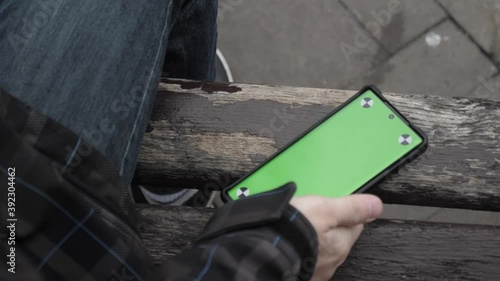 Young guy picks up the phone due to notifications, green screen, autumn, cold weather