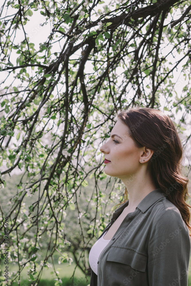 Portrait of a beautiful brunette under blooming tree branches in the garden. Spring time. Portrait of a beautiful brunette under blooming tree branches in the garden. Spring time.