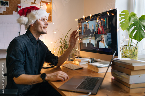 Young man having Zoom video call via a computer in the home office. Christmas Day party. Virtual happy hour wine Stay at home and work from home concept during Coronavirus pandemic. Man in santa hat