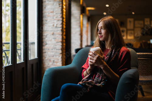 Nice blonde woman having a coffee sitting on a couch in a cafeteria looking out the window.
