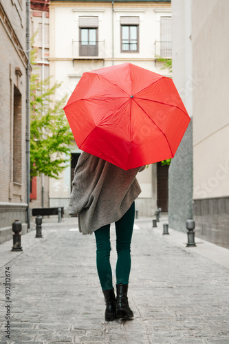 Fair blonde woman walking down the street with a red umbrella.