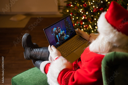 Happy mom and son talking to santa claus by video chat on a laptop. Woman and boy remotely wishes Merry Christmas photo