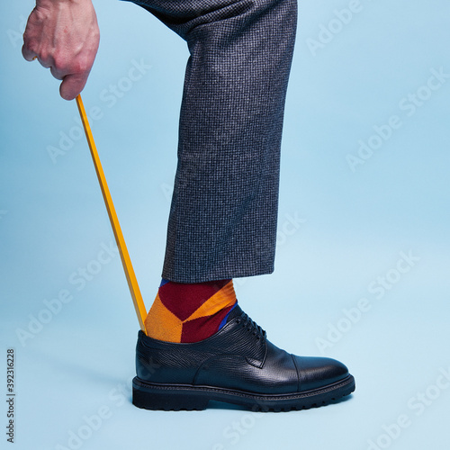 A man in handmade Italian leather shoes and colored funny socks puts on shoes using a shoe horn photo