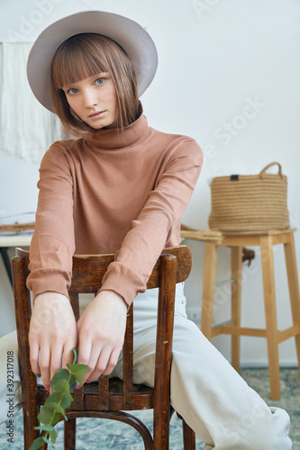Young beautiful girl in a gray hat sits on a chair at home photo