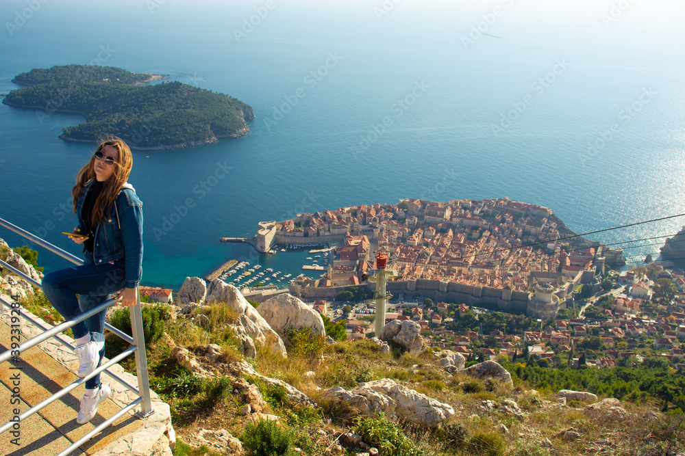 Φωτογραφία Attractive brunette traveller sitting on a railing above the city of Dubrovnik, viewpoint on Srd mountain