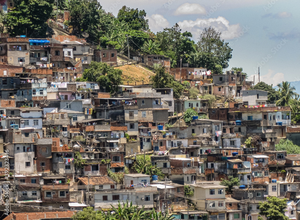 Rio de Janeiro, Brazil - December 24, 2008: Part of favela on mountain slope under blue cloudscape. Mass of poor houses on top of each other and some green foliage.