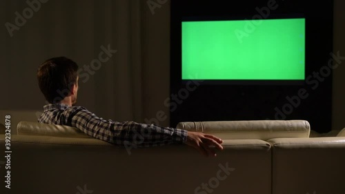 A young man is watching TV with a green screen