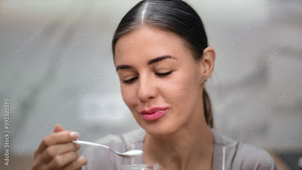 Closeup smiling face of young woman eating yogurt use spoon at kitchen. Shot with RED camera in 4K Closeup smiling face of young woman eating yogurt use spoon at kitchen. Shot with RED camera in 4K