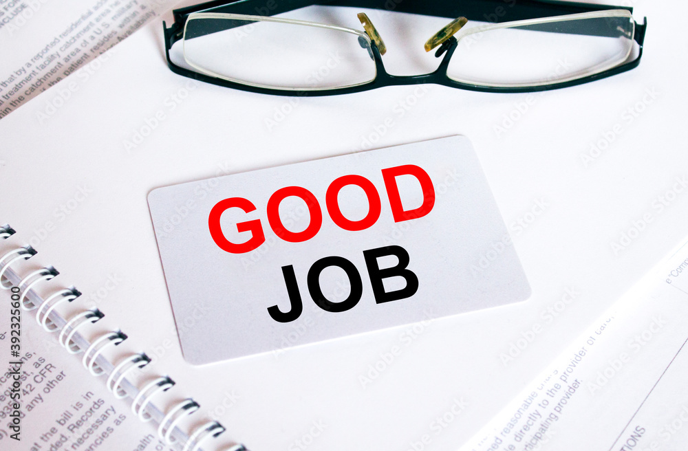 Text Good Job on a business card lying on a notepad with eyeglasses and text documents Text Good Job on a business card lying on a notepad with eyeglasses and text documents
