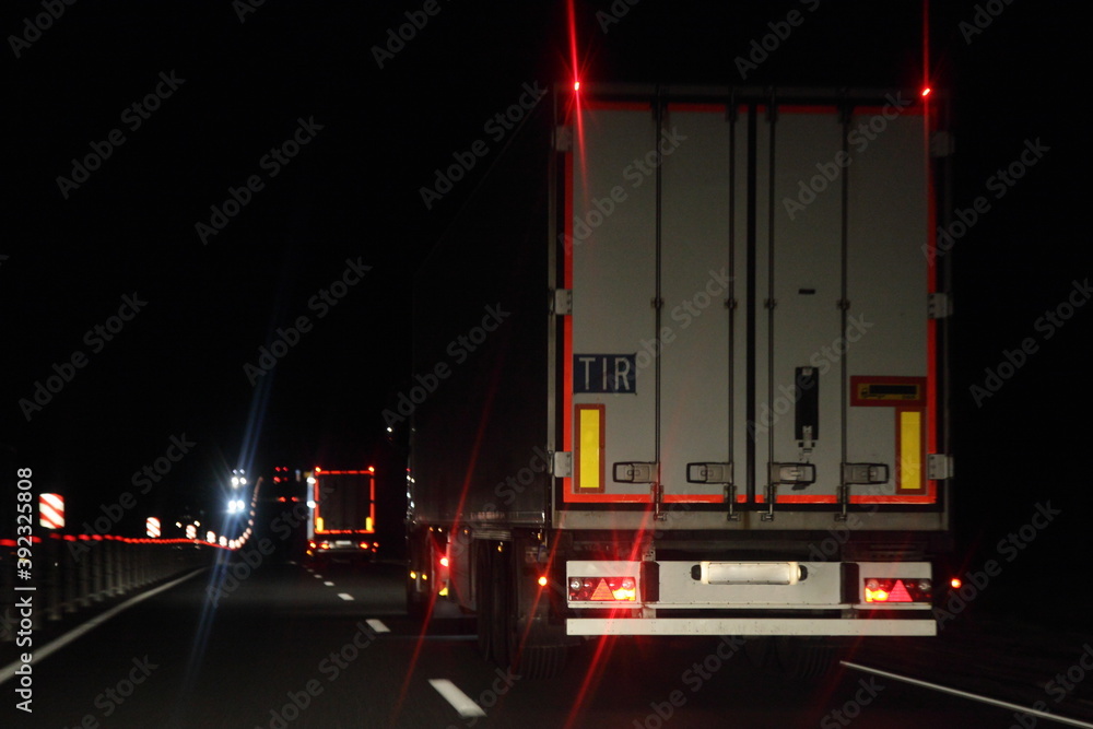Semi trailer truck with lighting reflection stripe and TIR sign on rear board move on dry asphalted night road in dark, back view - intrenational transportation logistics