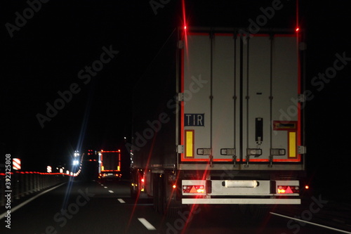 Obraz na płótnie Semi trailer truck with lighting reflection stripe and TIR sign on rear board move on dry asphalted night road in dark, back view - intrenational transportation logistics w salonie