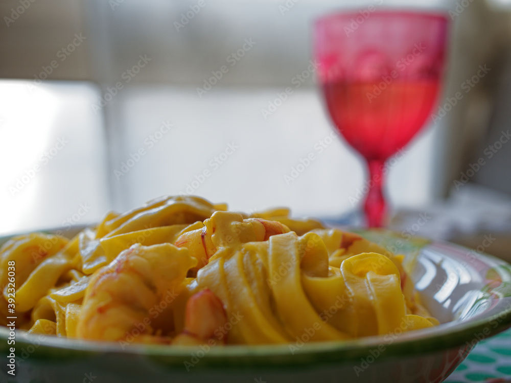Lunch time at home with the family with a first course based on fish. Pasta with saffron and prawns served on the table on a colorful plate. Lunch time at home with the family with a first course based on fish. Pasta with saffron and prawns served on the table on a colorful plate.