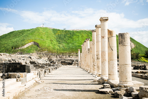 Columns lining the main street of the ancient Roman Decapolis ruins in Israel with a green hill in the background