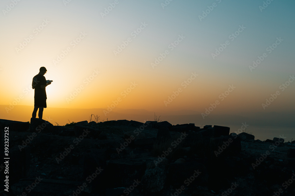 Silhouette of a man reading on a mountain at sunset
