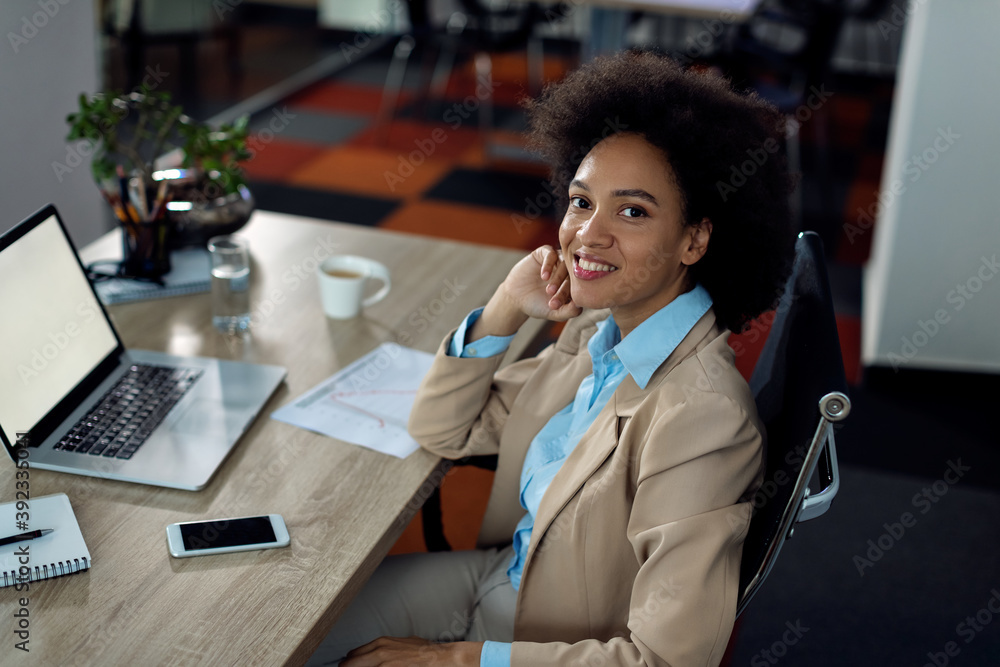 Happy African American businesswoman working on laptop in the office and looking at camera. Happy African American businesswoman working on laptop in the office and looking at camera.