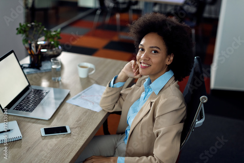 Happy African American businesswoman working on laptop in the office and looking at camera.
