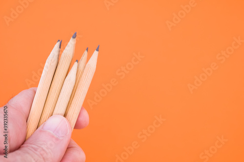 Closeup shot of a hand holding wooden pencils isolated on an orange background photo