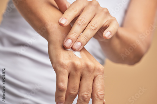 Close up shot of a woman using moisturizer hand cream while standing against beige background