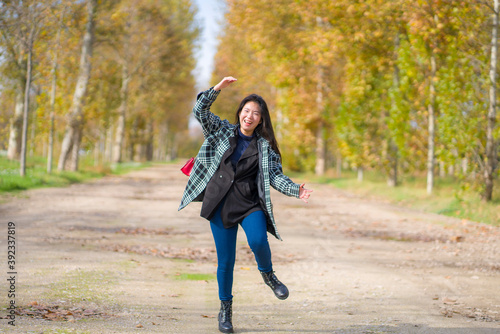 outdoors lifestyle portrait of young happy and pretty Asian Korean woman jumping carefree and cheerful at beautiful city park in vibrant yellow and orange Autumn tree leaves © TheVisualsYouNeed