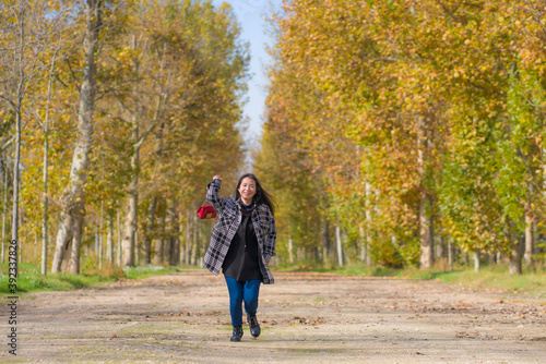 outdoors lifestyle portrait of young happy and pretty Asian Korean woman walking relaxed and cheerful at beautiful city park in vibrant yellow and orange Autumn tree leaves © TheVisualsYouNeed
