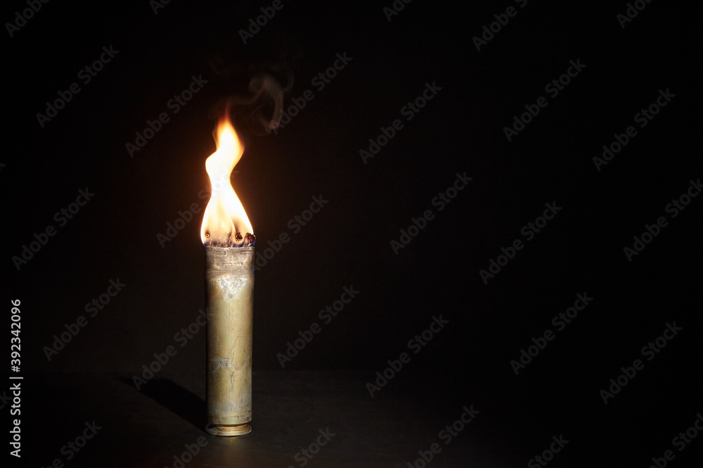 War candle. The candle burns in an empty sleeve. As a symbol of war and victims. Candle for remembering day. Located on black background. A candle used by the soldiers of the Second World War War candle. The candle burns in an empty sleeve. As a symbol of war and victims. Candle for remembering day. Located on black background. A candle used by the soldiers of the Second World War
