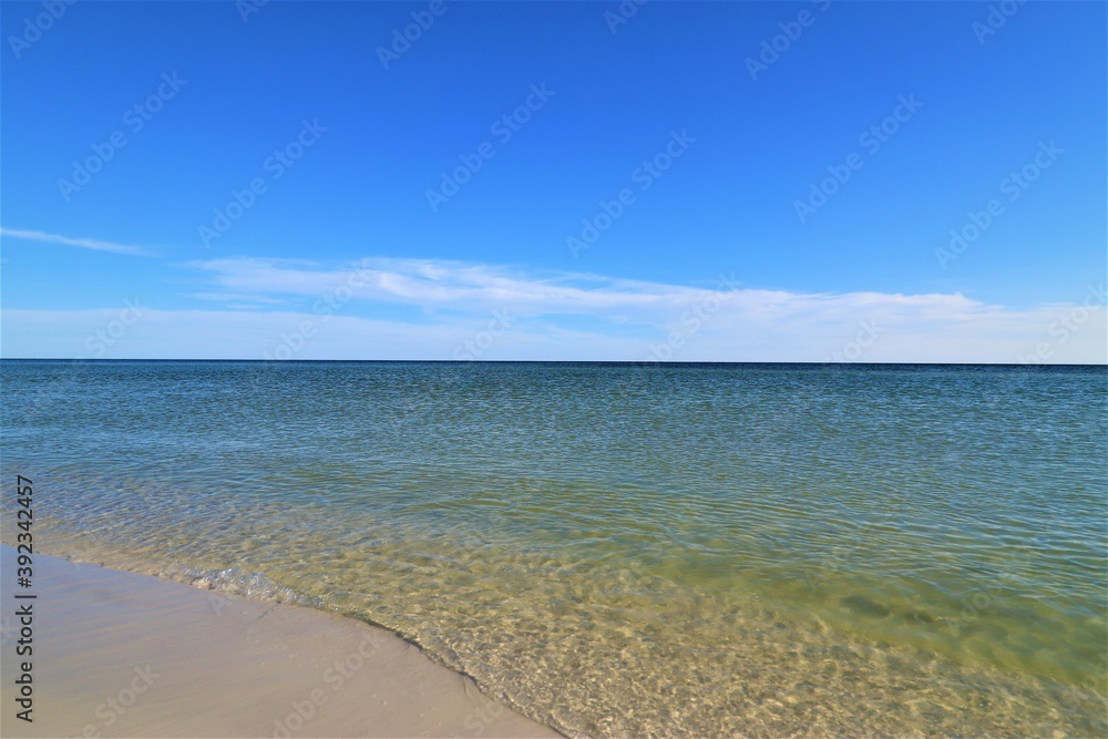 The seascape, a beautiful blank view from the coast of the Gulf of Mexico, calm ocean waters without waves over the horizon converge with a clear blue sky, in the foreground you can see the coast with