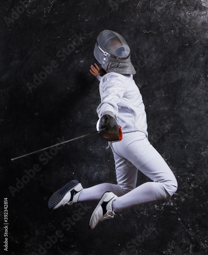 Foto Teenage girl fencer dressed in uniform with epee and helmet