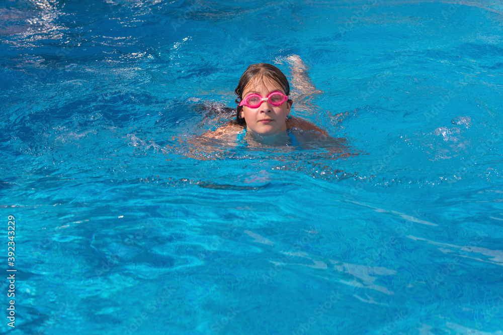 Girl in glasses swim in the blue swimming pool.