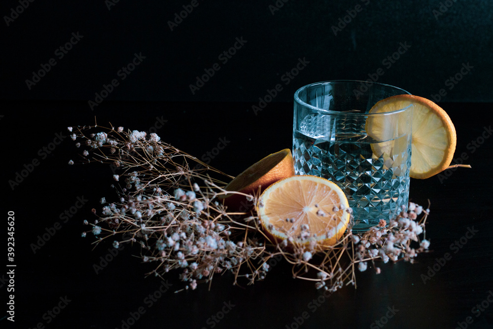Alcohol drink (gin and tonic cocktail) garnished with lemon fruit and flower isolated on black background. Iced cocktail drink with lemon and herbs. Alcohol drink (gin and tonic cocktail) garnished with lemon fruit and flower isolated on black background. Iced cocktail drink with lemon and herbs.