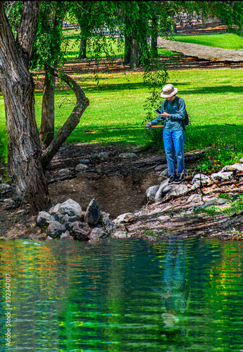 Fototapeta Naklejka Na Ścianę i Meble -  A picture of solitude fishing alone with a fishing pole in one hand and a cellphone in another landscape.