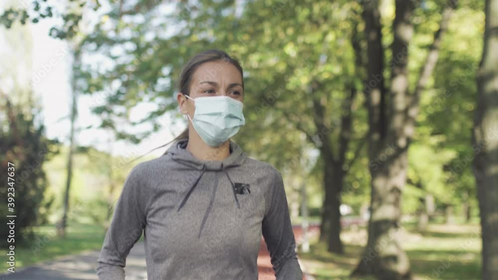 Fitness girl running on an all weather synthetic track surface in the park. Wearing protective face mask. Sport during pandemic Fitness girl running on an all weather synthetic track surface in the park. Wearing protective face mask. Sport during pandemic