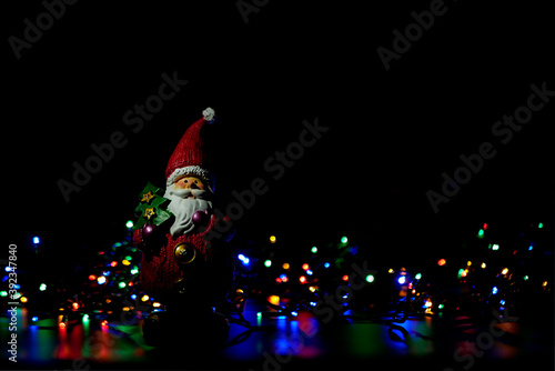 Figure of Santa Claus among the colourful Christmas lights on black background.