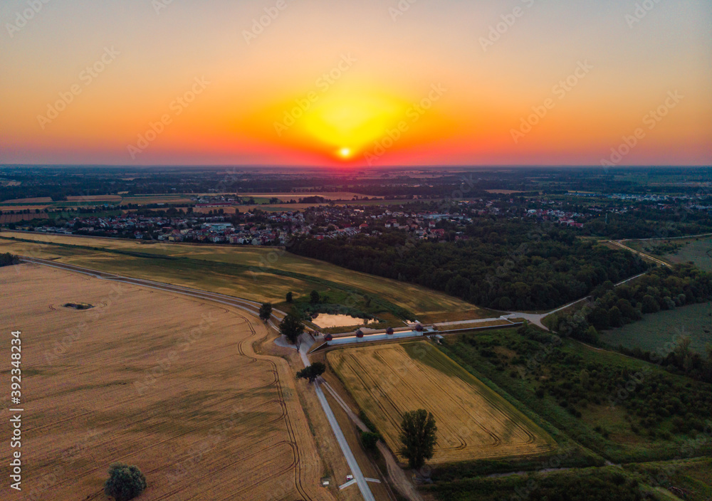 Aerial view to rising sun over fields village and forest at morning