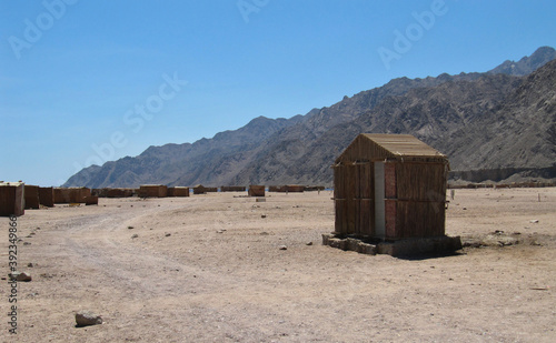 Lonely house and shacks near a dirt road against the backdrop of the Sinai Mountains. A gray ridge of mountains in a blue sky haze