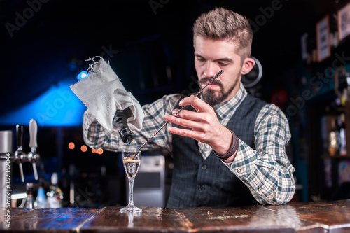 Bearded bartending pouring fresh alcoholic drink into the glasses while standing near the bar counter in nightclub photo