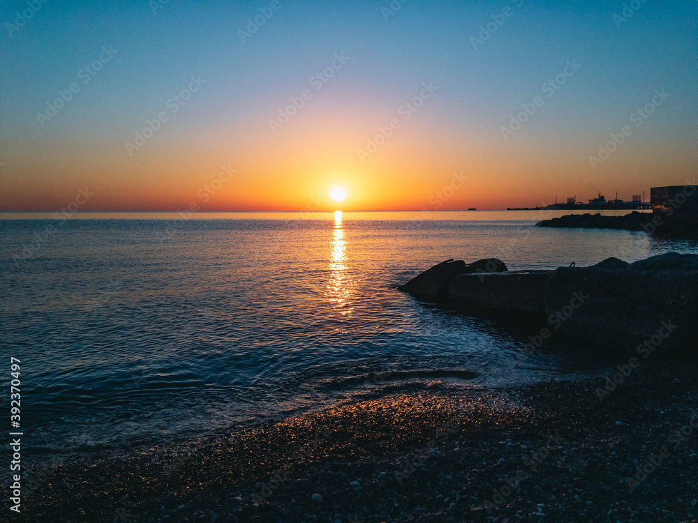 Beautiful colorful sunset with the sun setting beyond the horizon. Waves by the sea with the reflection of sun rays on the water. View of a calm and relaxing seascape at sunset.