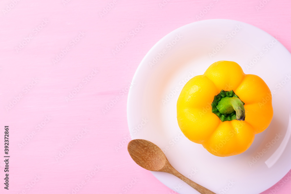 Fototapeta Yellow bell pepper on white plate with wooden spoon on pink background, Top view